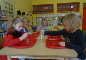Dzieci siedzą przy stoliku, w ręce trzymają pipetki, które napełniają wodą i przelewają do pojemników z drożdżami.
